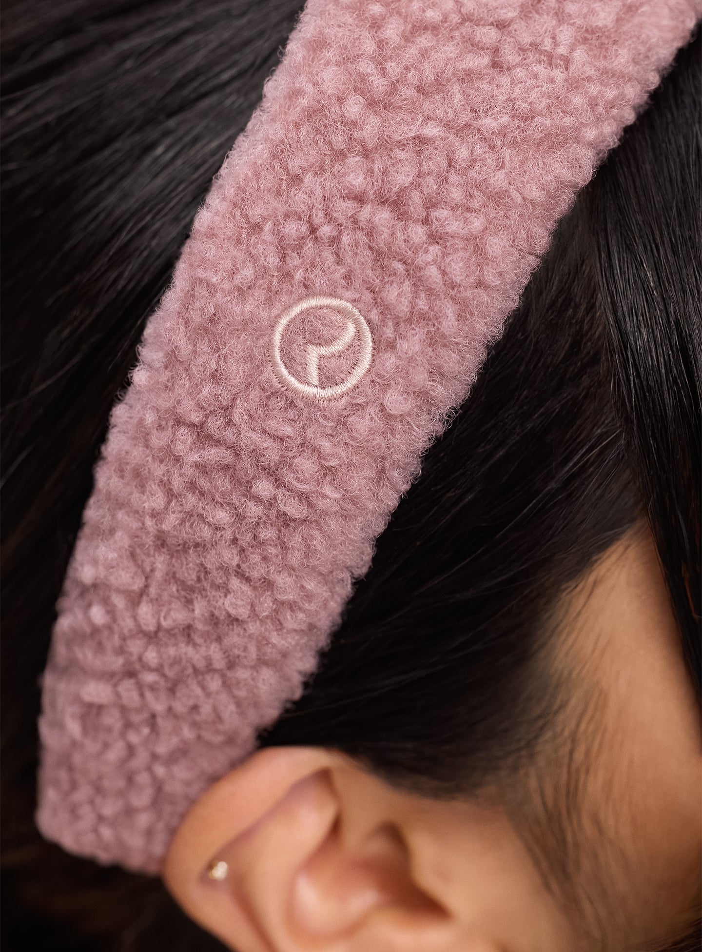 A close-up of the Rare Beauty logo on Rare Beauty's Find Comfort Headband, which is worn by a model with black hair.