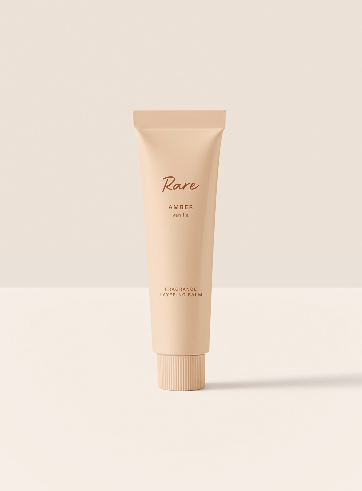 The Rare Amber Vanilla Fragrance Layering Balm stands upright in its minimalist light orange packaging.