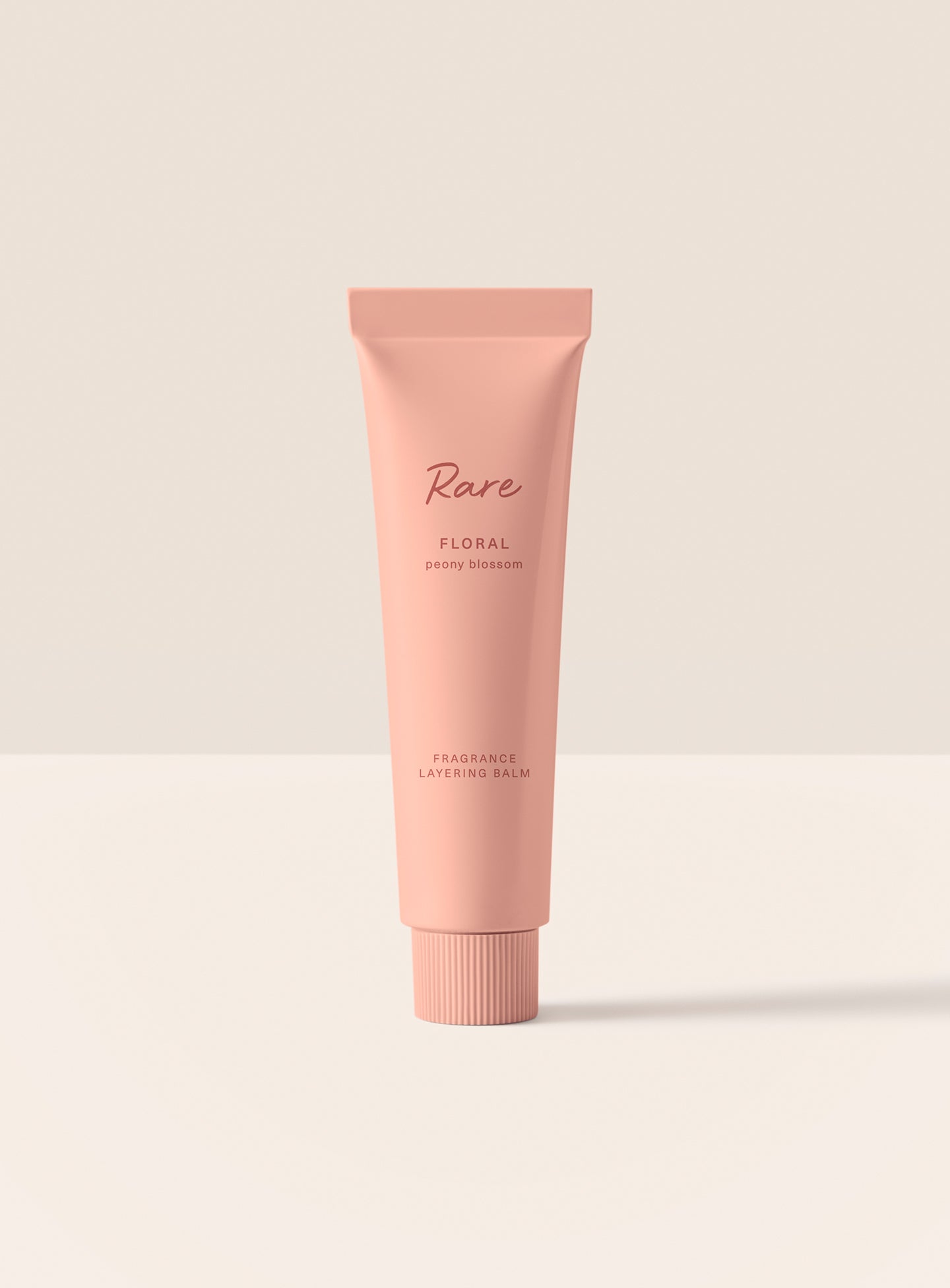 The Rare Floral Peony Fragrance Layering Balm stands upright in its minimalist green packaging.
