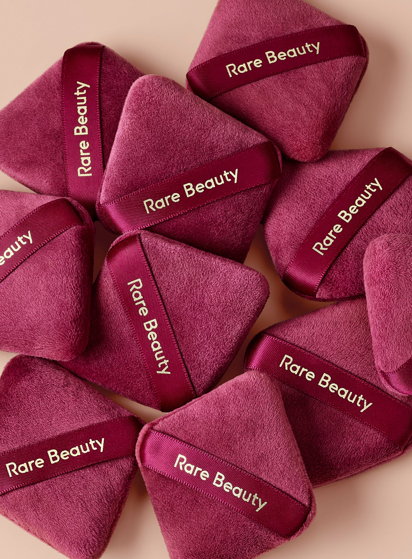 A group of Rare Beauty's Soft Touch Powder Puffs lay on a soft pink background. 