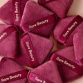 A group of Rare Beauty's Soft Touch Powder Puffs lay on a soft pink background. 