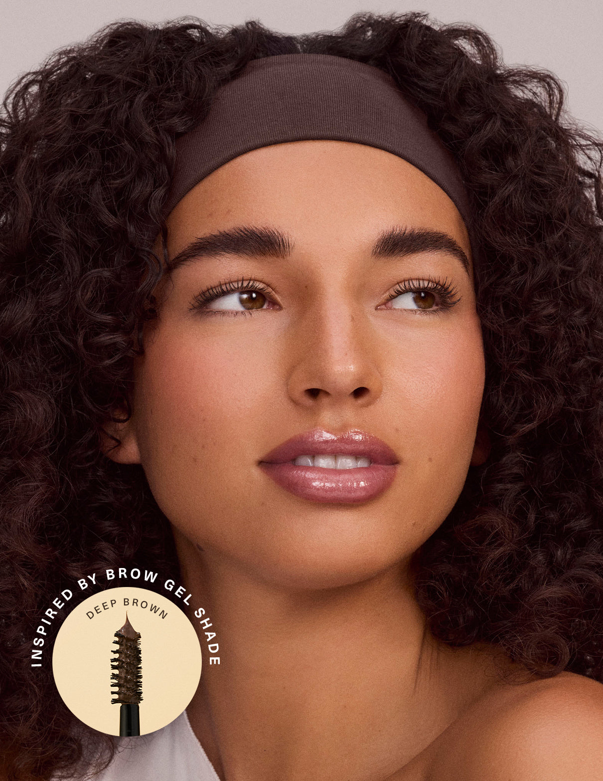 Female model with dark curly hair wearing a brown headband, with a brand logo in the corner.