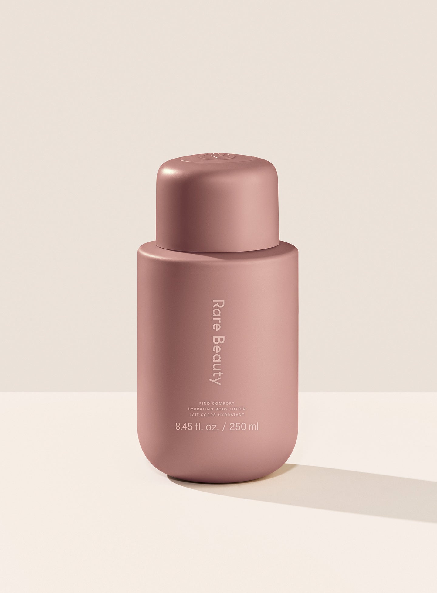 Rare Beauty's Find Comfort Hydrating Body Lotion standing on a white table against a white background.