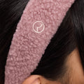 A close-up of the Rare Beauty logo on Rare Beauty's Find Comfort Headband, which is worn by a model with black hair.