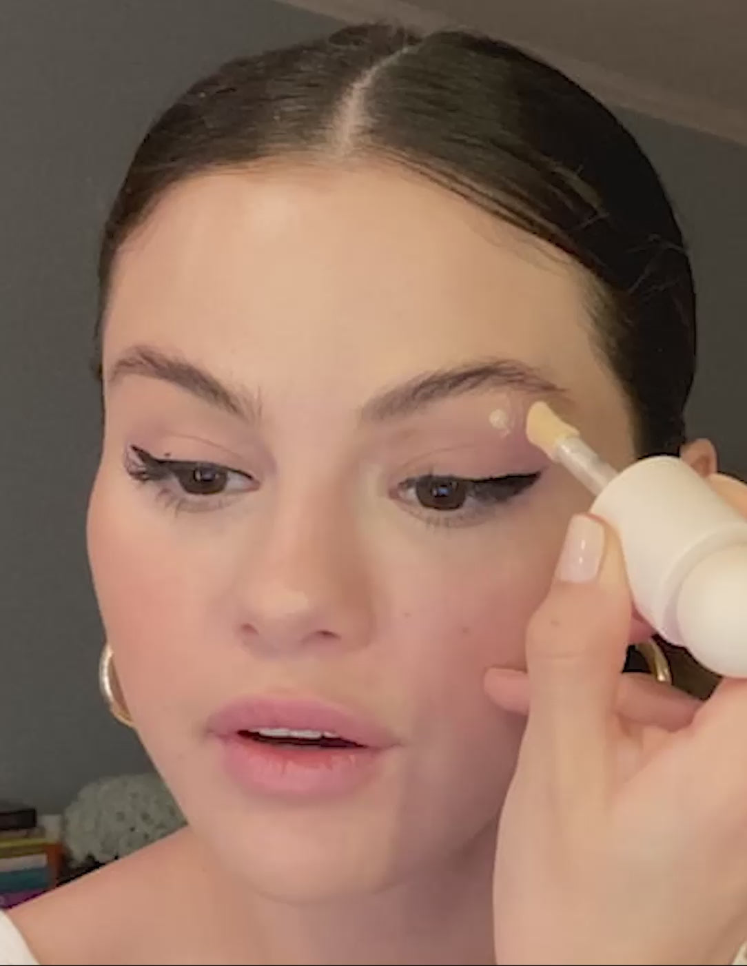Selena Gomez wearing winged eyeliner applying Positive Light Liquid Luminizer below her eyebrow.