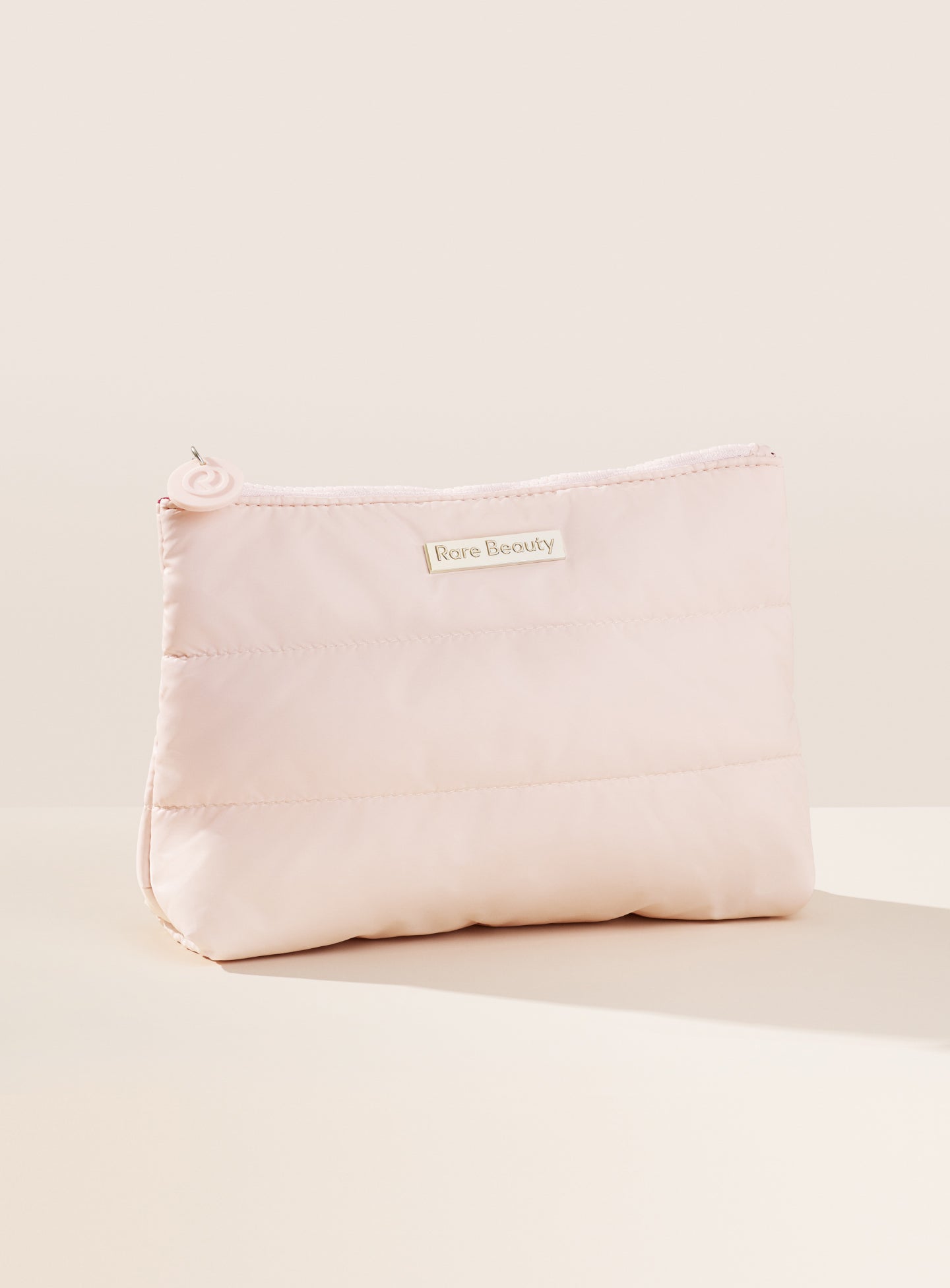 The outside of the Puffy Makeup Bag by Rare Beauty in soft peach.